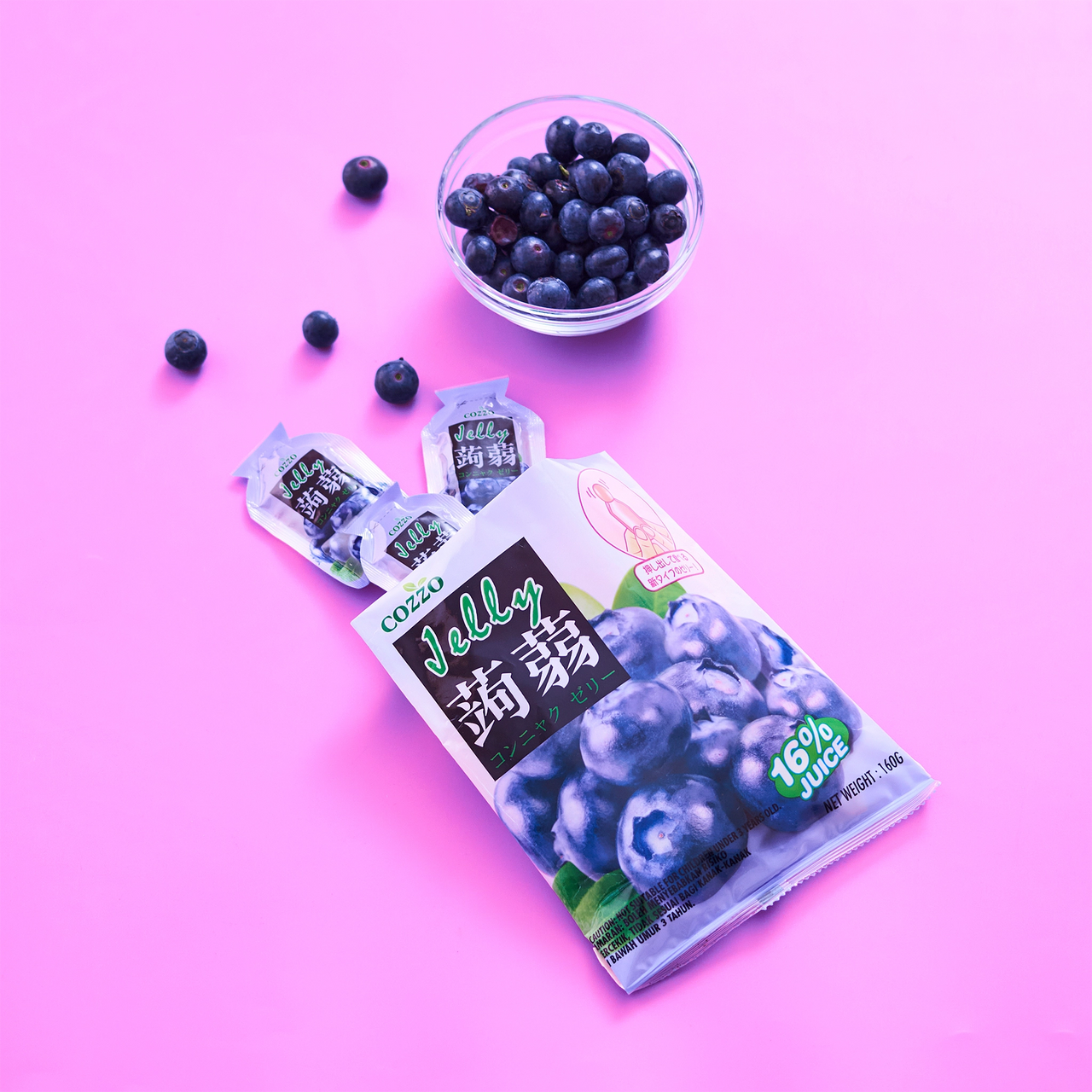 Plant-based candy alternative Cozzo konnyaku jelly blueberry flavour pouch on a bright pink background, two mini jelly pouches beside it, and a glass bowl filled with fresh blueberries above, with a “16% juice” badge, 160g.

بديل نباتي للحلويات — كيس جيلي كوننياكو Cozzo بنكهة التوت الأزرق على خلفية وردية، وبجانبه عبوتان صغيرتان، وفوقه وعاء زجاجي مليان توت أزرق، مع شارة “16% عصير”، الوزن 160غ.