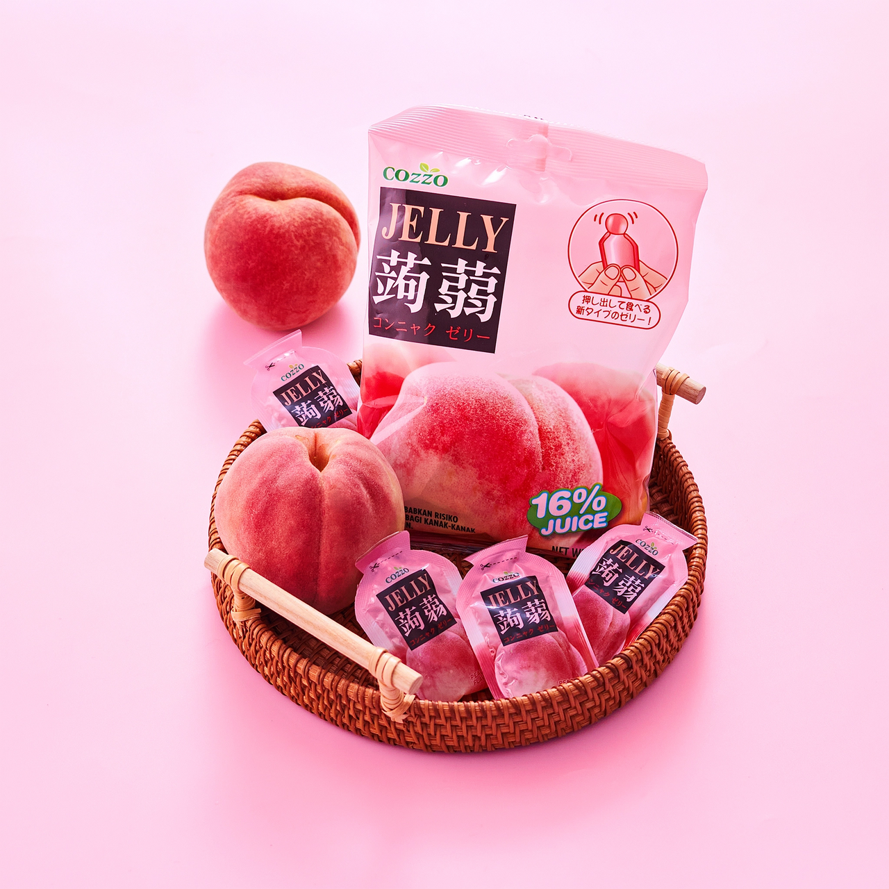 Fruit jelly snack Cozzo konnyaku jelly peach flavour pouch standing in a woven basket on a pink background, surrounded by whole peaches and several mini peach jelly pouches, showing a “16% juice” badge, 160g.

جيلي فواكه — كيس جيلي كوننياكو Cozzo بنكهة الخوخ داخل سلة خوص على خلفية وردية، حوله حبات خوخ كاملة وعدة عبوات صغيرة من جيلي الخوخ، مع شارة “16% عصير”، الوزن 160غ.